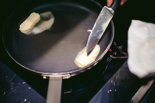 woman housewife prepares fried eggs with ham and vegetables in his kitchen. spreads the butter in the pan