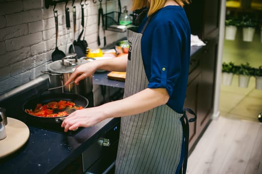 woman housewife prepares fried eggs with ham and vegetables in his kitchen. cut peppers and tomatoes, and puts them in a frying pan