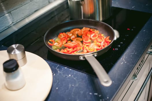 woman housewife prepares fried eggs with ham and vegetables in his kitchen. cut peppers and tomatoes, and puts them in a frying pan