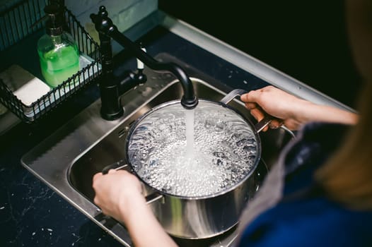 woman housewife in the kitchen. girl collects water from the tap in the pan