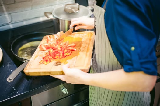 woman housewife prepares fried eggs with ham and vegetables in his kitchen. cut peppers and tomatoes, and puts them in a frying pan