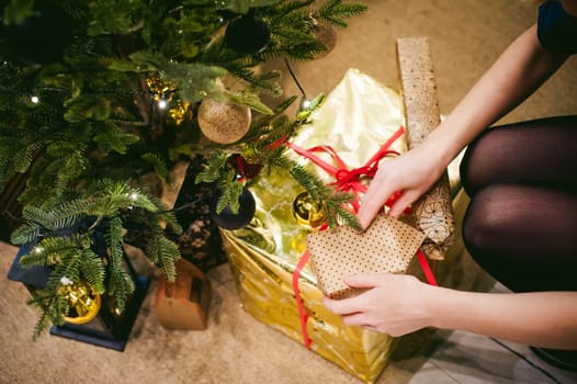 Women's hands are laid out gifts under the tree. girl decorates a festive Christmas tree, balls and toys Ornamental, at home in the cozy atmosphere of holiday