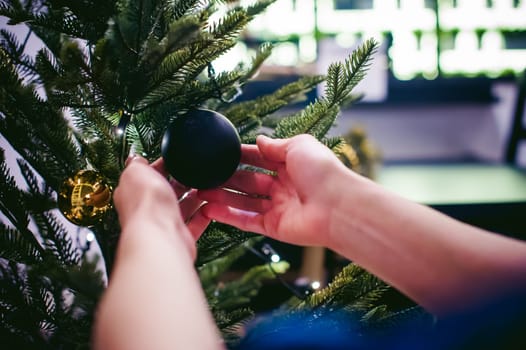 Female hands decorating a Christmas tree. girl decorates a festive Christmas tree, balls and toys Ornamental, at home in the cozy atmosphere of holiday
