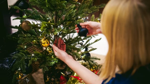 Female hands decorating a Christmas tree. girl decorates a festive Christmas tree, balls and toys Ornamental, at home in the cozy atmosphere of holiday