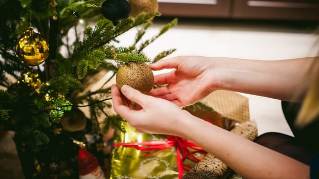 Female hands decorating a Christmas tree. girl decorates a festive Christmas tree, balls and toys Ornamental, at home in the cozy atmosphere of holiday