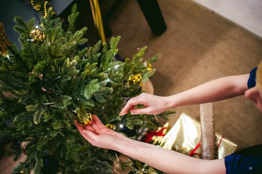 Female hands decorating a Christmas tree. girl decorates a festive Christmas tree, balls and toys Ornamental, at home in the cozy atmosphere of holiday