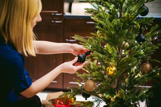 Female hands decorating a Christmas tree. girl decorates a festive Christmas tree, balls and toys Ornamental, at home in the cozy atmosphere of holiday