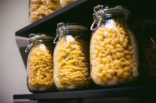 pasta in the jar. on kitchen shelves are different kinds of pasta in glass jars