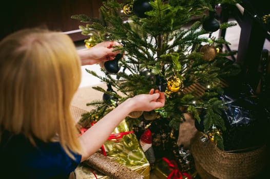 Female hands decorating a Christmas tree. girl decorates a festive Christmas tree, balls and toys Ornamental, at home in the cozy atmosphere of holiday