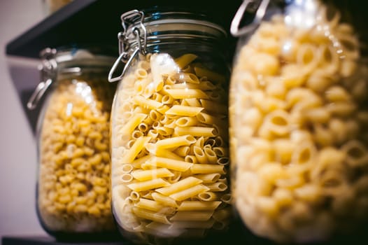 pasta in the jar. on kitchen shelves are different kinds of pasta in glass jars