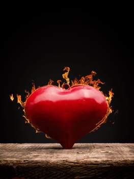 Burning heart, red metal heart shape with flames on a wooden table, love or Valentines Day concept background