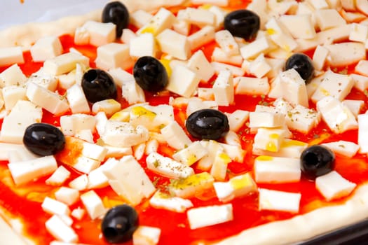 Raw pizza decorated mozzarella, black olives and tomato sauce ready to be baked