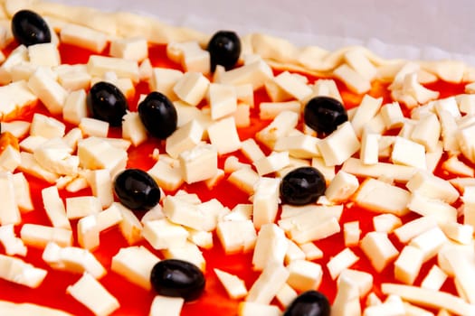 Raw pizza decorated mozzarella, black olives and tomato sauce ready to be baked
