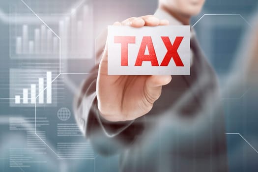 Businessman holding a card with Tax text over blue background