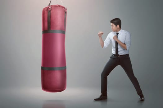 Young asian businessman punching boxing bag over gray background