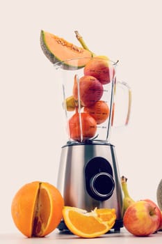 blender with a lot of fruits in front of white background