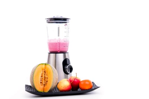 blender with milkshake and a lot of fruits in front of white background