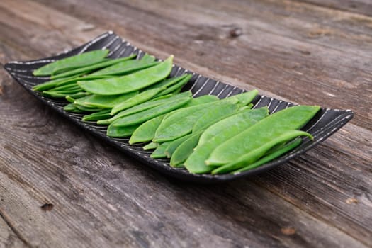 elongated bowl with green peapods  on wooden ground