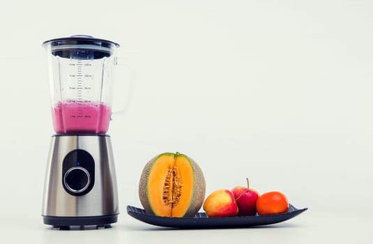 blender with milkshake and a lot of fruits in front of white background
