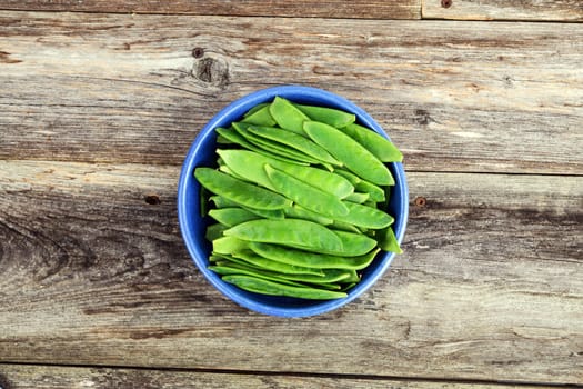 blue bowl with green peapods from above on wooden ground