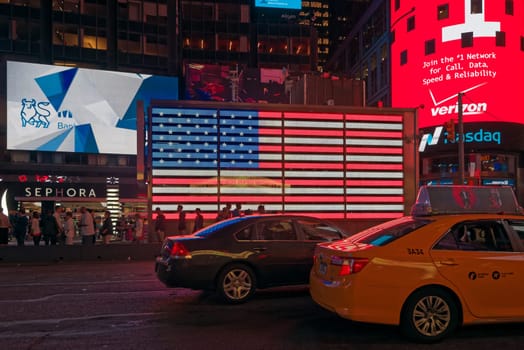 New York, USA - june 06, 2015: Time Square at night. Signage lights illuminate the road. A flag of the USA shines with its colors. Taxis, cars and people passing. Time Square, New York.
