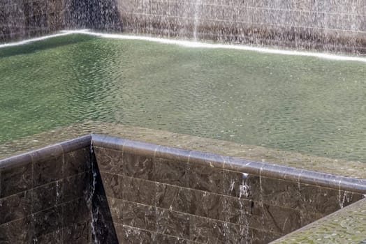 New York, USA - June 08, 2015: South pool memorial commemorating the victims of the 11 september terror attack in 2001. New York architecture in the background.