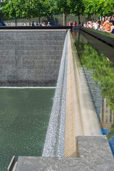 New York, USA - June 08, 2015: South pool memorial commemorating the victims of the 11 september terror attack in 2001. New York architecture in the background.