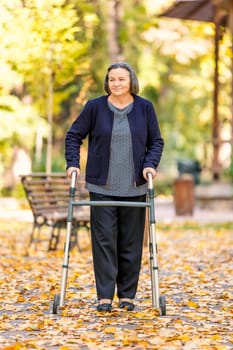 Senior woman with walker walking outdoors in autumn park.