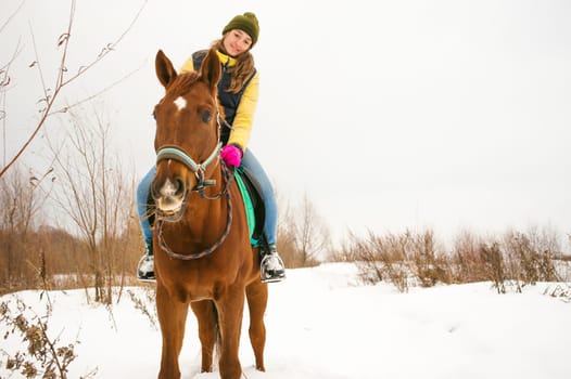 Woman in winter clothes is riding on a horse on a background of white snow.