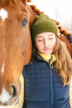 Woman in winter clothes and the horse stand together against the white snow. love and care for horses. animal portrait on a white background.