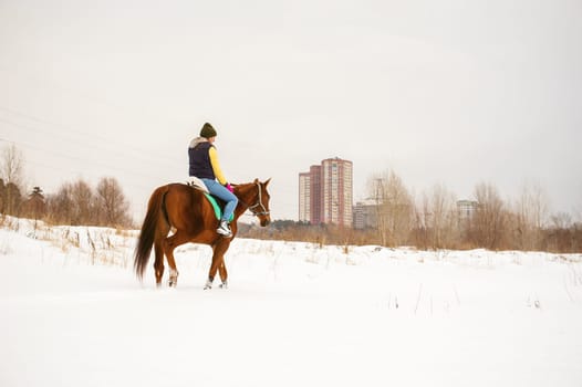 Woman in winter clothes is riding on a horse on a background of white snow.