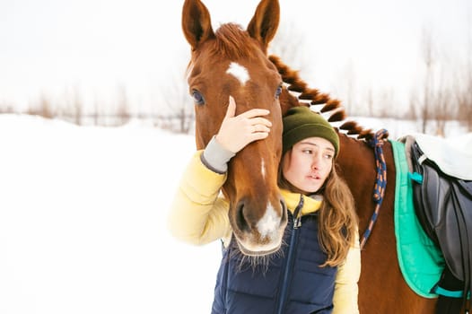 Woman in winter clothes and the horse stand together against the white snow. love and care for horses. animal portrait on a white background.