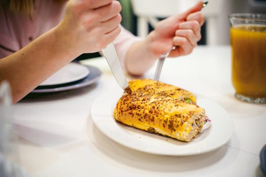 Pretty blonde woman in pink shirt, eating at home fork and knife. breakfast sandwich and peach juice. on white table in bright interior of kitchen in plate sandwich juice poured in glass. Close up