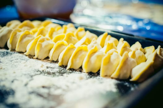hand modeling dumplings at home in the kitchen. pelmeni lay on a baking sheet