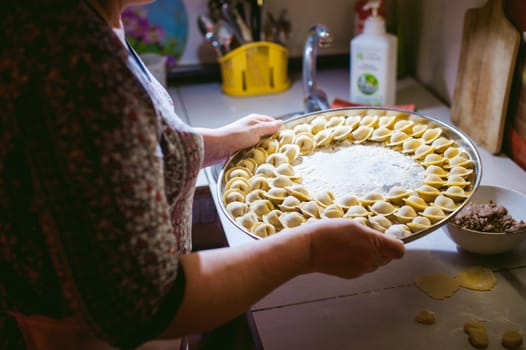 hand modeling dumplings at home in the kitchen. pelmeni lay on a baking sheet