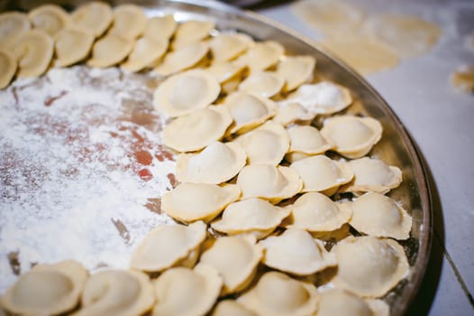 hand modeling dumplings at home in the kitchen. pelmeni lay on a baking sheet