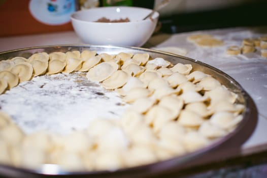 hand modeling dumplings at home in the kitchen. pelmeni lay on a baking sheet