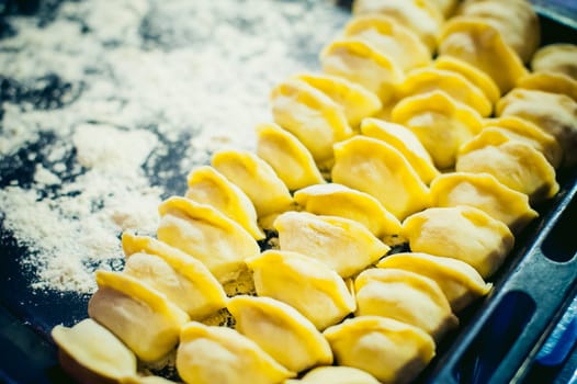 hand modeling dumplings at home in the kitchen. pelmeni lay on a baking sheet