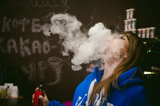 young Cute woman, the seller in vape shop shop, smoking electronic cigarette,  vaping and releases a cloud of vapor