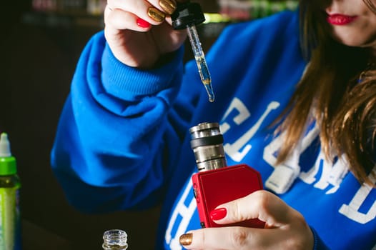 young Cute woman, the seller in vape shop shop, smoking electronic cigarette,  fills the tank juice