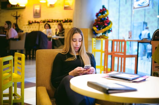 woman in a cafe. young girl sitting at a table in a black dress and looking into the smartphone
