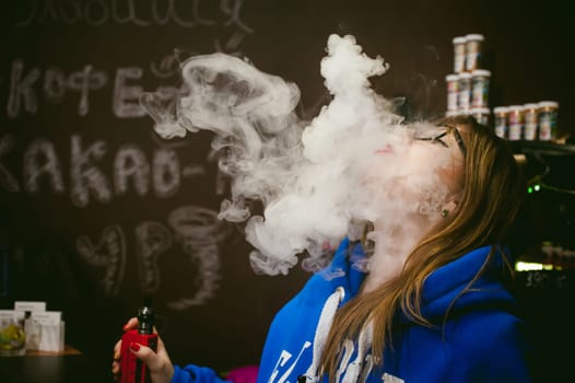 young Cute woman, the seller in vape shop shop, smoking electronic cigarette,  vaping and releases a cloud of vapor