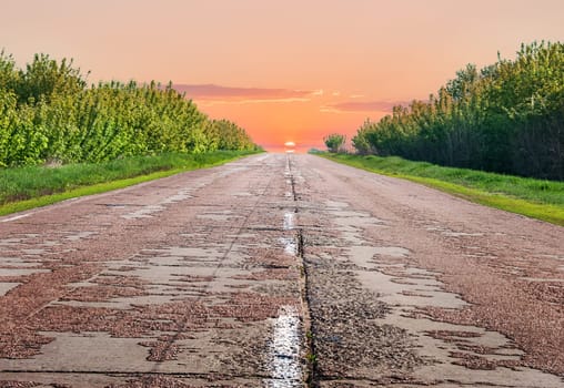 Old highway in the evening. The sun is ahead of the horizon.