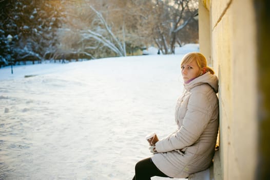 young woman dressed in warm clothes drinking takeaway coffee from the cup on the street in winter