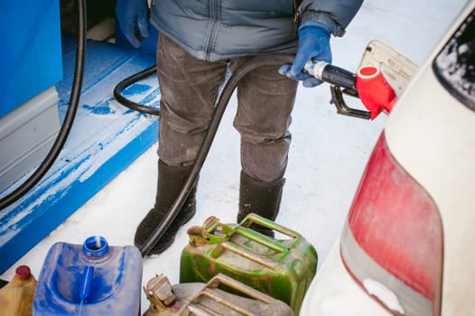 adult man fills a car with petrol at a fuel station in the winter. refueling nozzle man holding in his hand, pouring the liquid in the canister and fuel tank