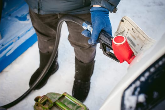 adult man fills a car with petrol at a fuel station in the winter. refueling nozzle man holding in his hand, pouring the liquid in the canister and fuel tank