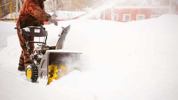 man operating snow blower to remove snow on driveway