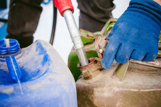 adult man fills a car with petrol at a fuel station in the winter. refueling nozzle man holding in his hand, pouring the liquid in the canister and fuel tank