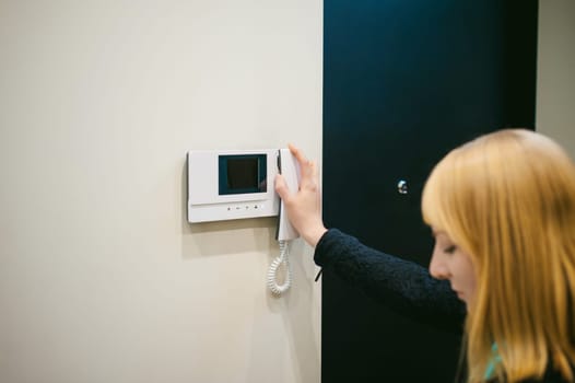 blonde woman hangs up the phone after answering the intercom call in her apartment