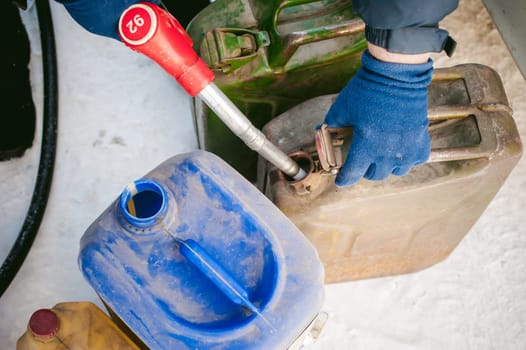 adult man fills a car with petrol at a fuel station in the winter. refueling nozzle man holding in his hand, pouring the liquid in the canister and fuel tank